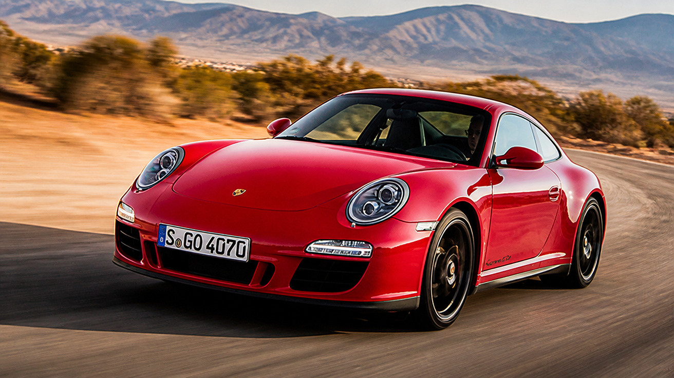 Red Porsche 911 sports car driving on a desert road with mountains in the background.