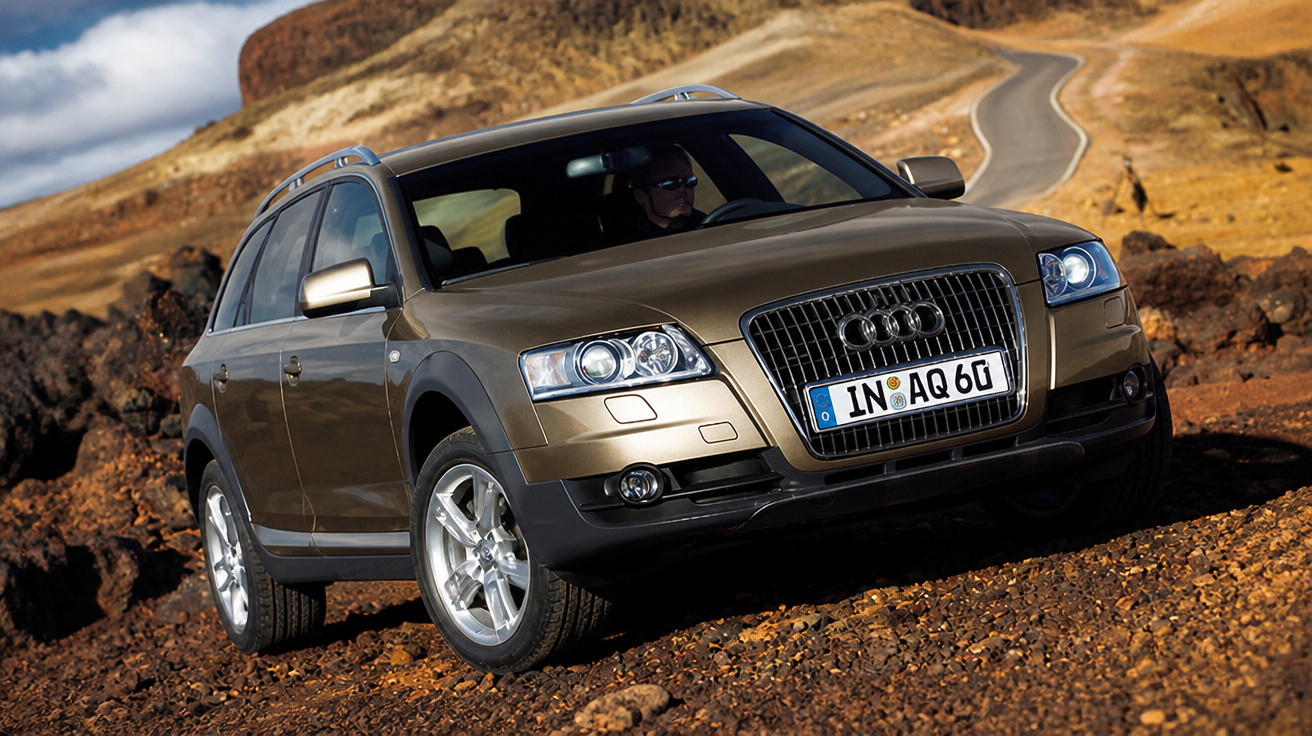 Brown Audi allroad quattro parked on rocky terrain with winding road and hills in the background