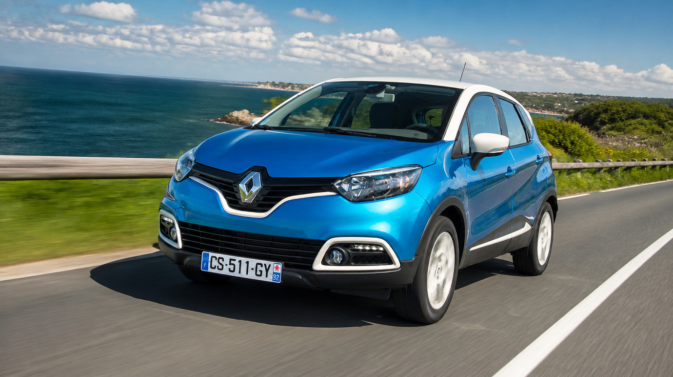 Blue Renault Captur compact SUV driving on a coastal road under a partly cloudy sky.