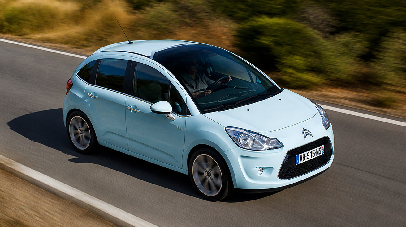 Light blue Citroën hatchback driving on a winding road with blurred background and dry grass.