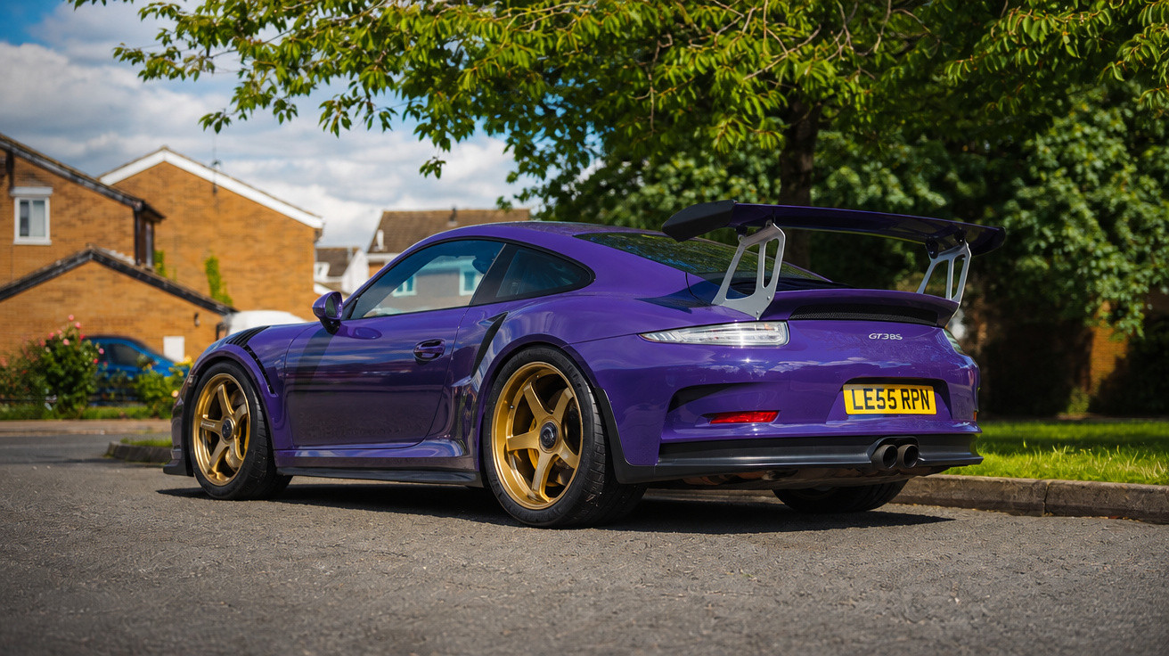 Purple Porsche 911 GT3 RS with gold wheels parked on a residential street under a tree on a sunny day.