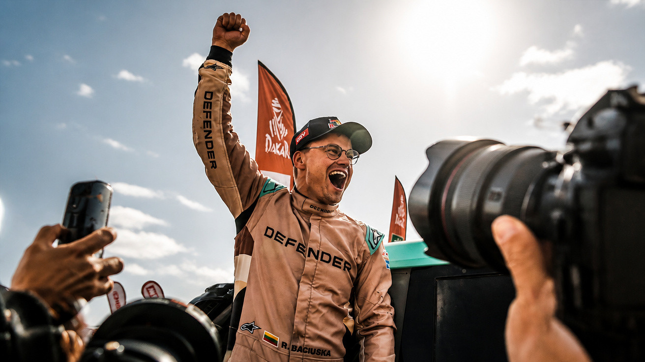 Race car driver celebrating victory with fist raised amid photographers and Dakar flags in background