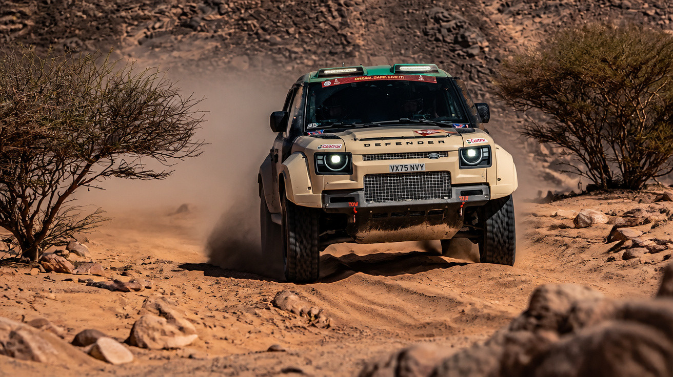 Beige Land Rover Defender racing on a rocky desert trail kicking up dust.